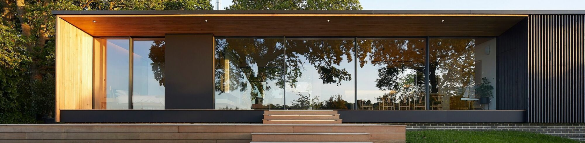 Une maison moderne avec de grandes baies vitrées, une façade en bois et une terrasse couverte